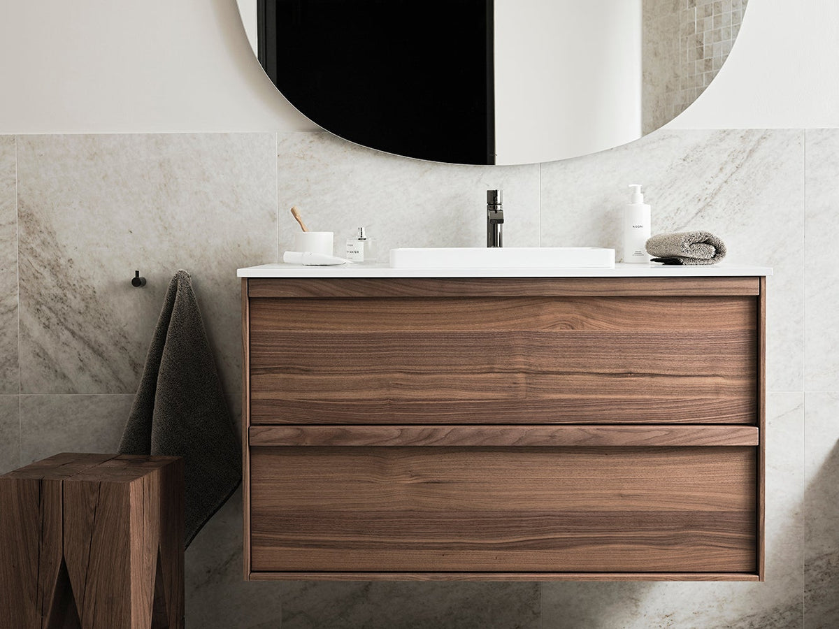 Haven H2 kommod i Walnut Wood med porslinstvättställ och oval spegel i ett badrum med marmorkakel